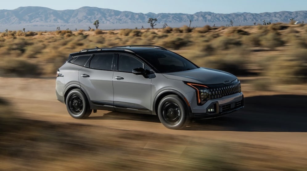 A gray 2026 Kia Sportage SUV driving down a dirt road in the desert