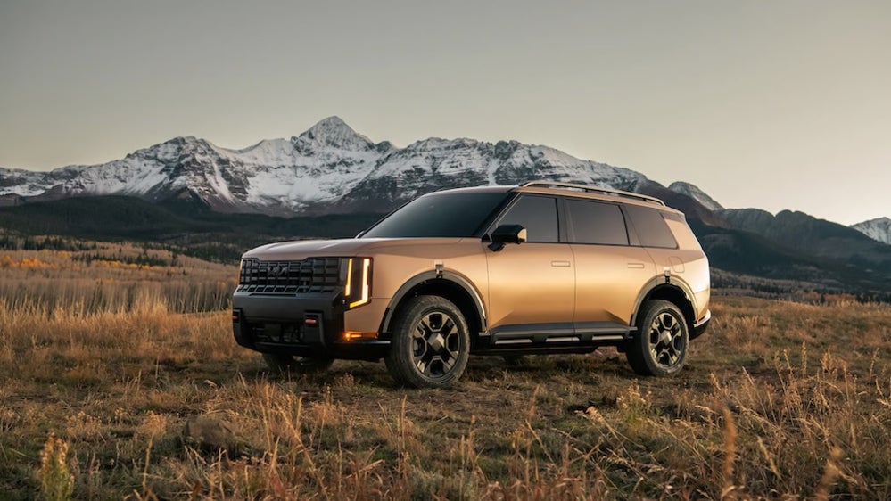 A brown 2027 Kia Telluride SUV parked in a field with mountains in the distance