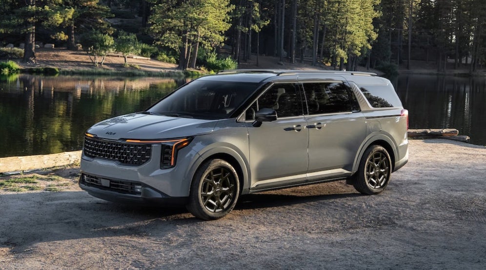 A gray 2027 Kia Carnival minivan parked by a lake