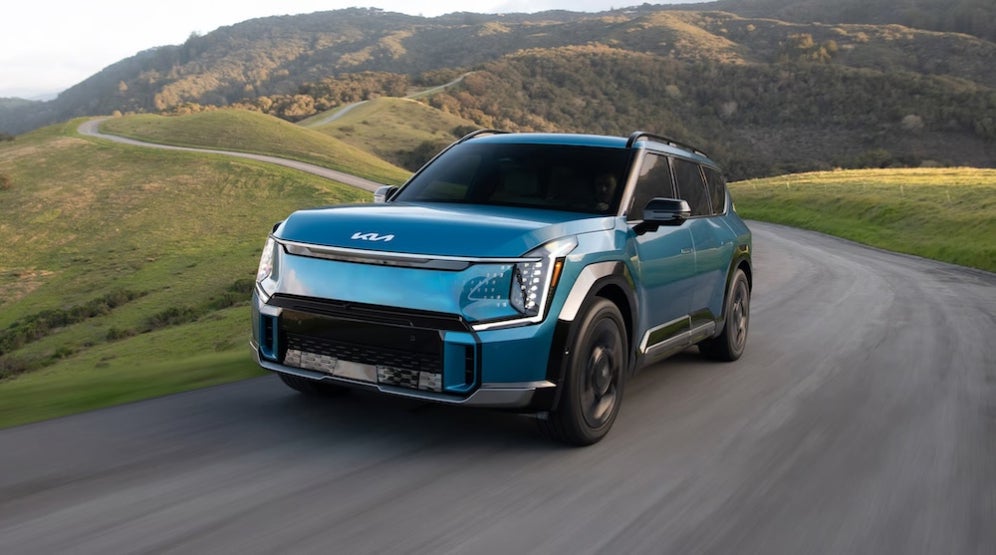 A bright blue Kia EV9 SUV on a mountain road