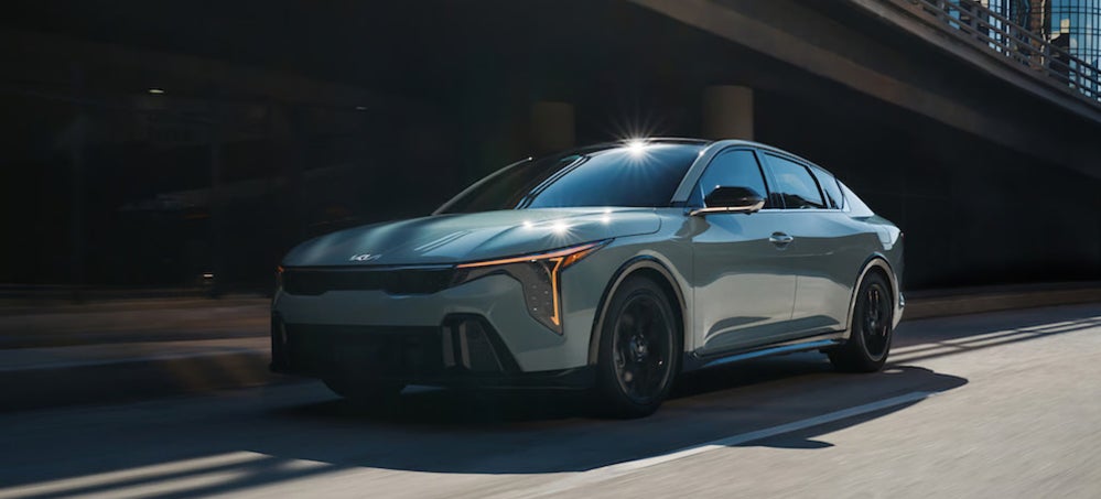 A light-colored 2025 Kia K4 sedan driving down a city street