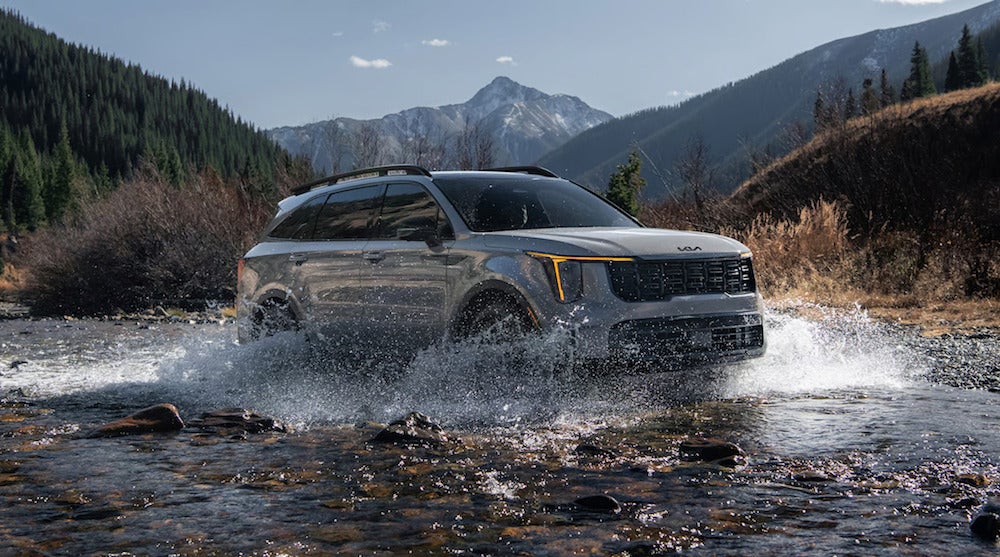 A gray 2026 Kia Sorento SUV driving through a shallow riverbed, splashing up water