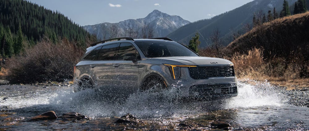 A silver 2026 Kia Sorento SUV driving through a mountain stream, with water splashing up on either side