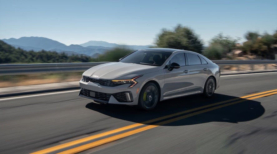 A gray 2026 Kia K5 sedan driving down a road