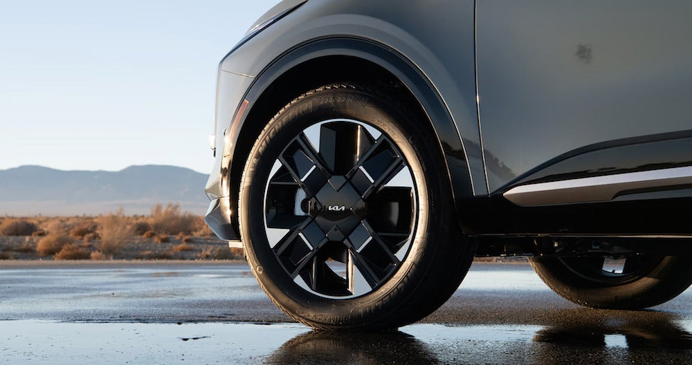 A closeup of the tires of a gray Kia Sportage Hybrid, with the desert in the background