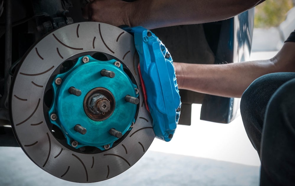 The arms of a white person working on a vehicle’s brakes