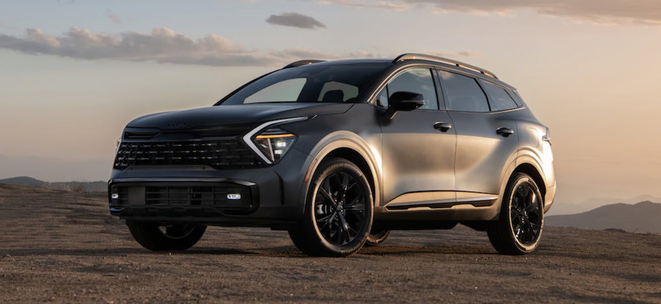 A three-quarters view of a dark-colored 2025 Kia Sportage Plug-In Hybrid SUV at sunset
