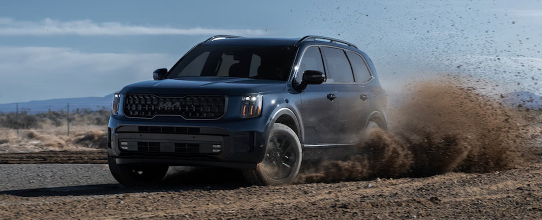 A dark-colored 2025 Kia Telluride SUV driving down a muddy road