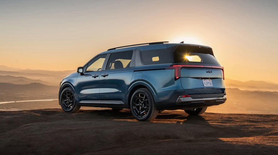 A blue 2026 Kia Carnival parked on a desert ledge at sunset