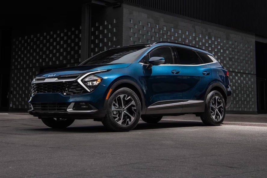 A dark blue 2025 Kia Sportage Hybrid SUV parked in front of a black wall